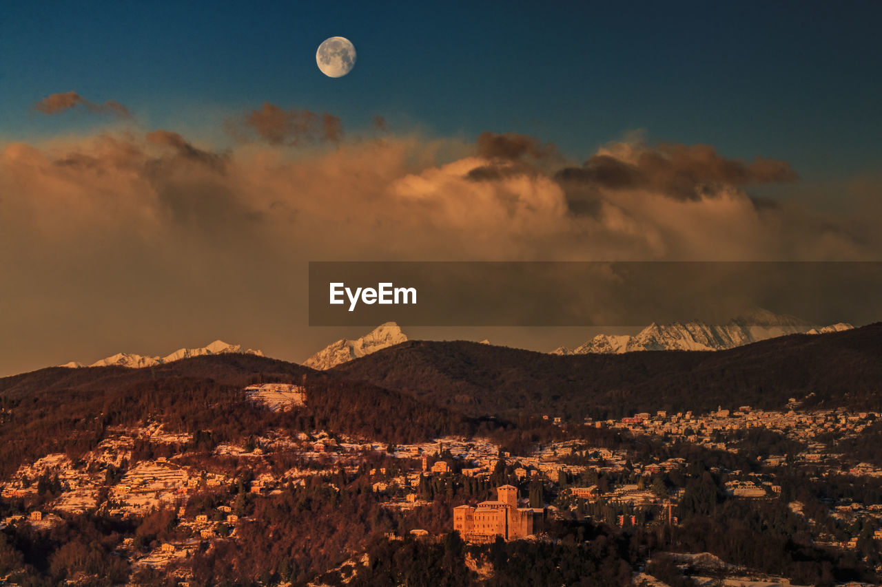 Townscape by mountains against cloudy sky during sunrise