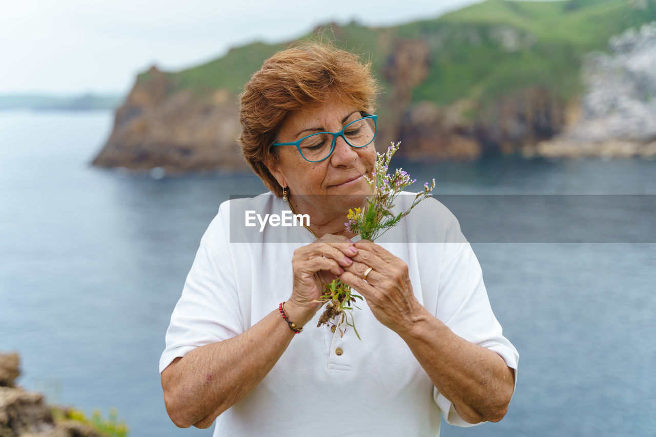 Senior woman smelling flowers against sea