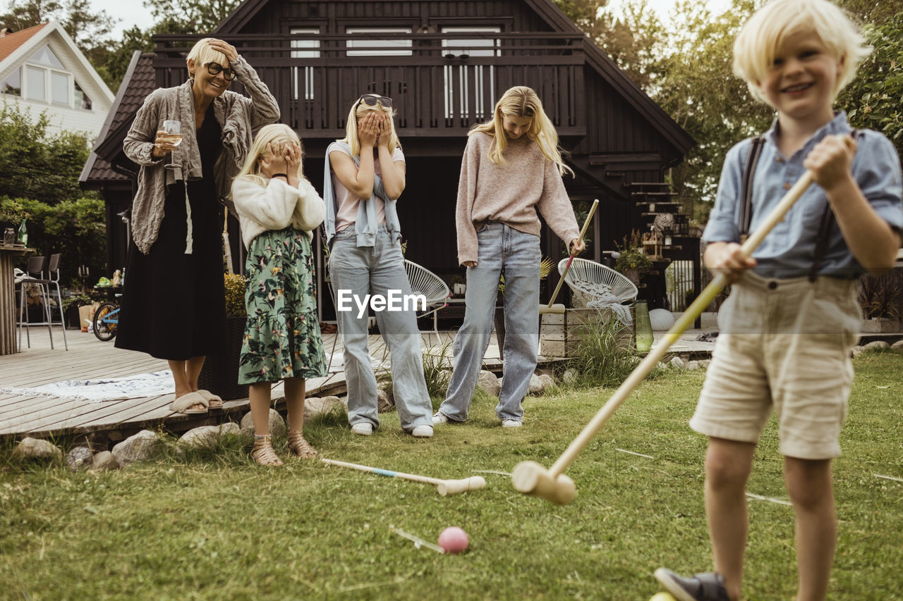 Boy with polo mallet standing by family in back yard at evening