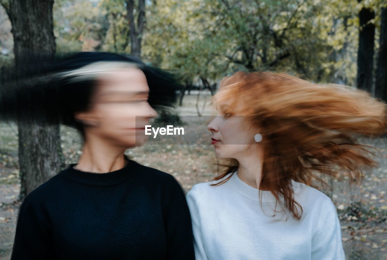 Lesbian couple shaking heads while standing against trees in park