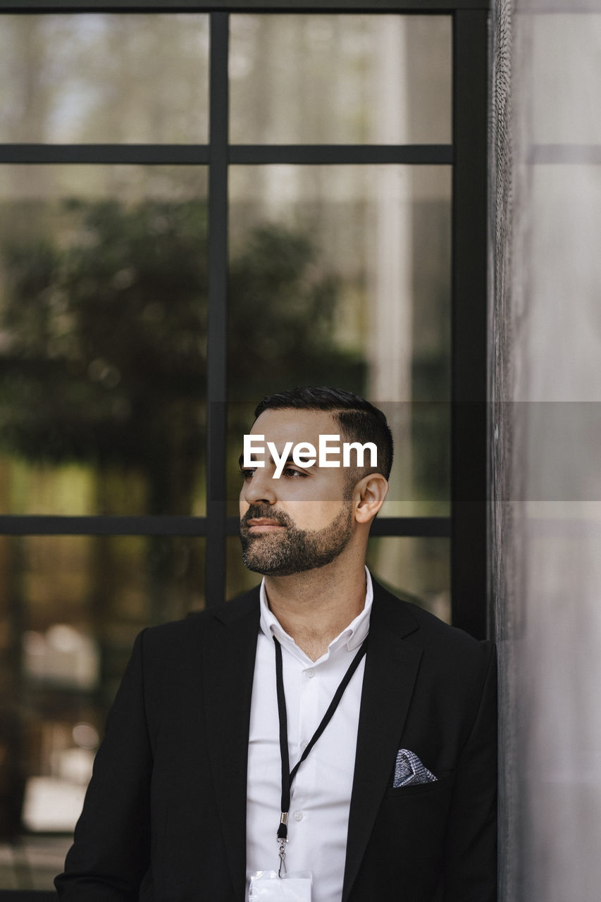 Businessman looking away while standing in front of glass wall