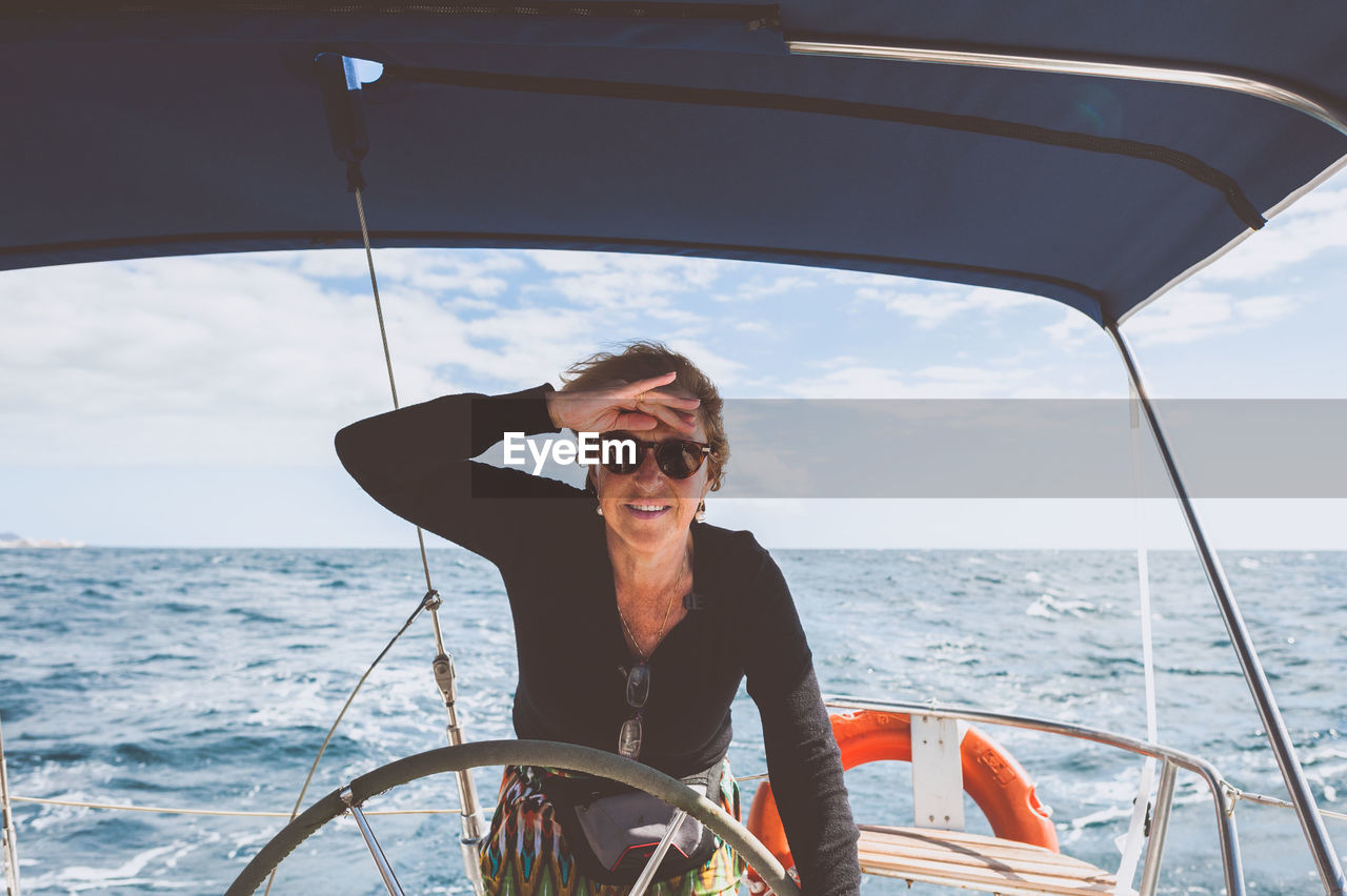 Portrait of smiling mature woman standing in boat on sea