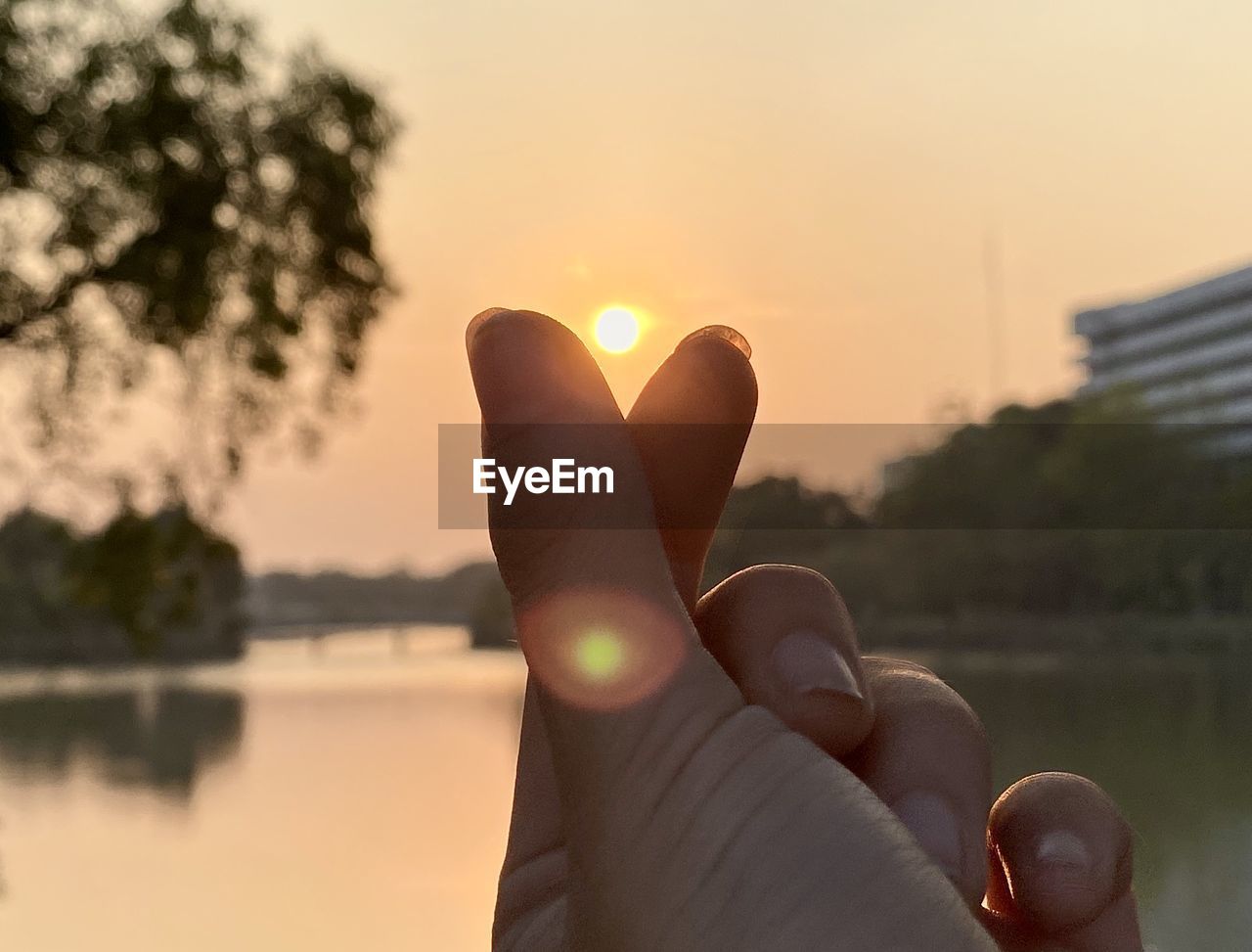 Close-up of hand against lake during sunset