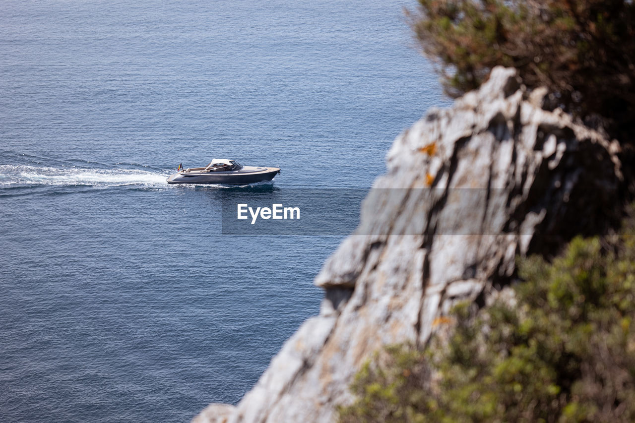 water, nautical vessel, transportation, mode of transportation, sea, coast, nature, day, ship, shore, beauty in nature, high angle view, cliff, terrain, scenics - nature, travel, sailing, vehicle, no people, outdoors, motion, boat, rock, bay, mountain, plant, tranquility, land, tranquil scene, wake, watercraft, on the move