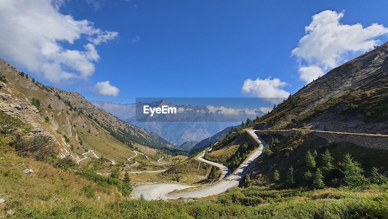 mountain, sky, mountain range, scenics - nature, environment, landscape, cloud, beauty in nature, mountain pass, nature, land, plant, travel destinations, travel, valley, tranquility, tranquil scene, no people, non-urban scene, road, blue, walking, day, outdoors, grass, tourism, adventure, tree, ridge, idyllic, pinaceae, plateau, mountain peak, architecture, pine tree, transportation, sunlight, forest, activity, snow, coniferous tree, rural scene, panoramic, green, social issues, vacation