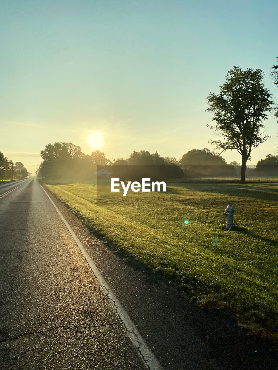 VIEW OF ROAD AMIDST FIELD AGAINST SKY DURING SUNSET