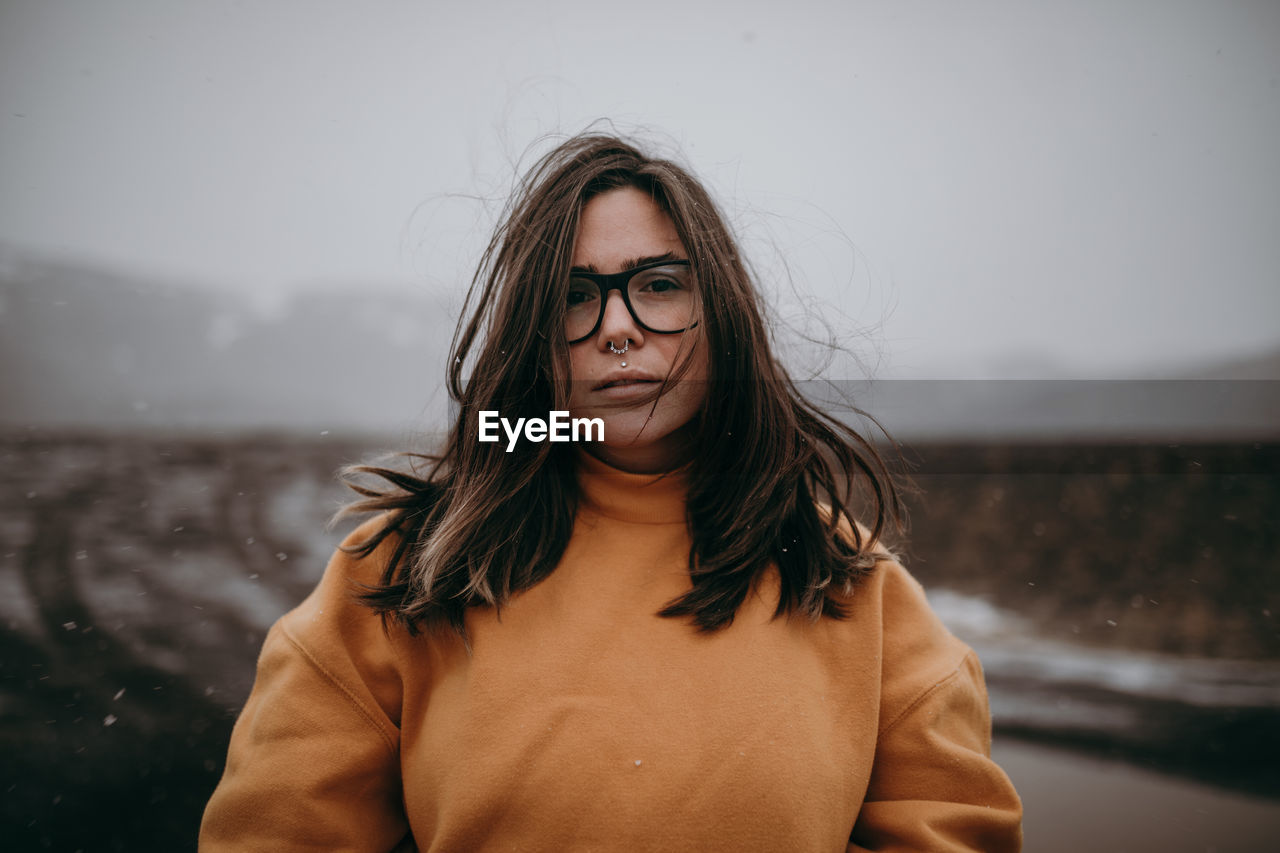 Young happy tourist in eyeglasses with piercing looking at camera between deserted ground in snow