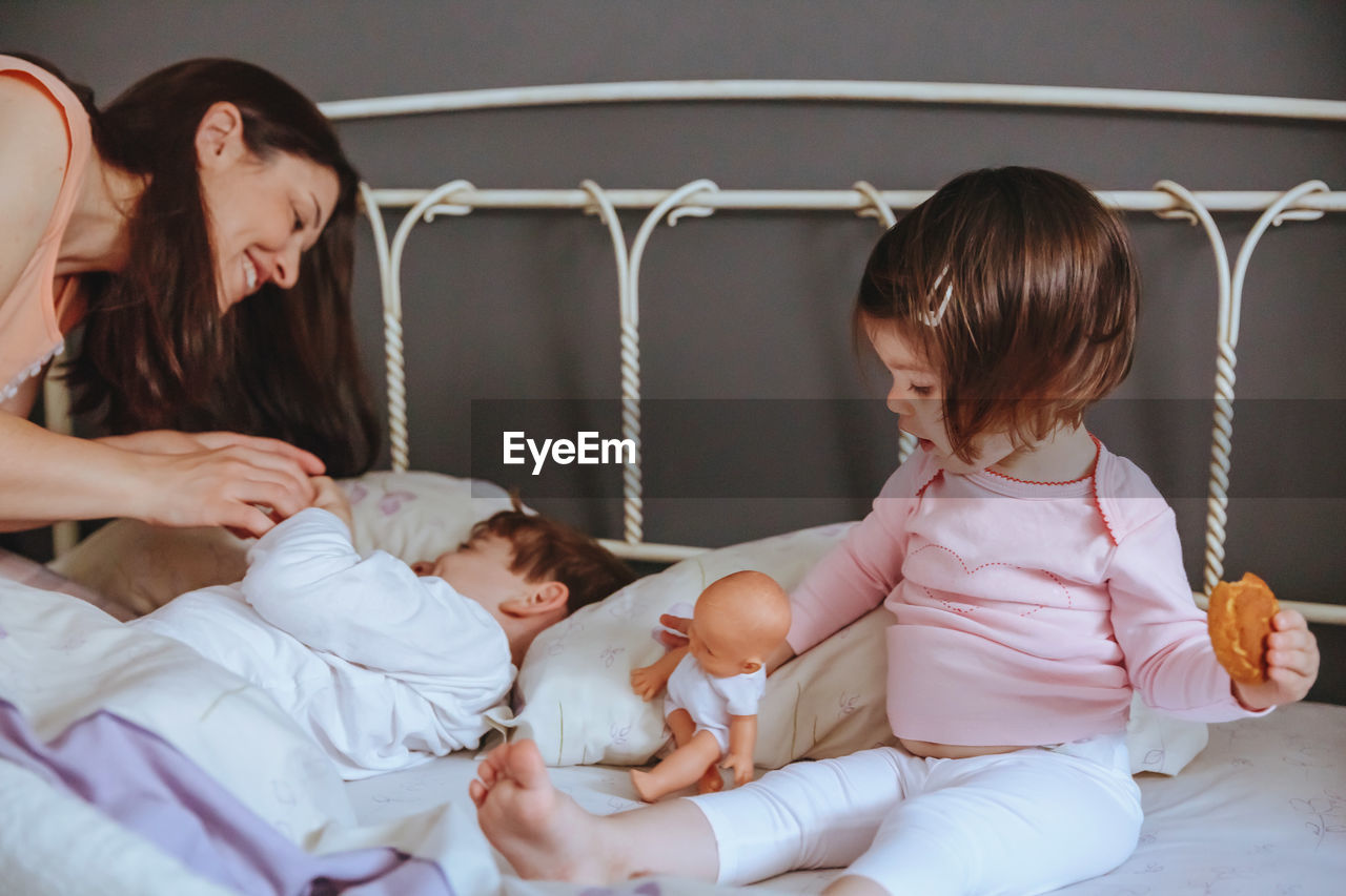 Cheerful mother playing with son and daughter while lying on bed at home