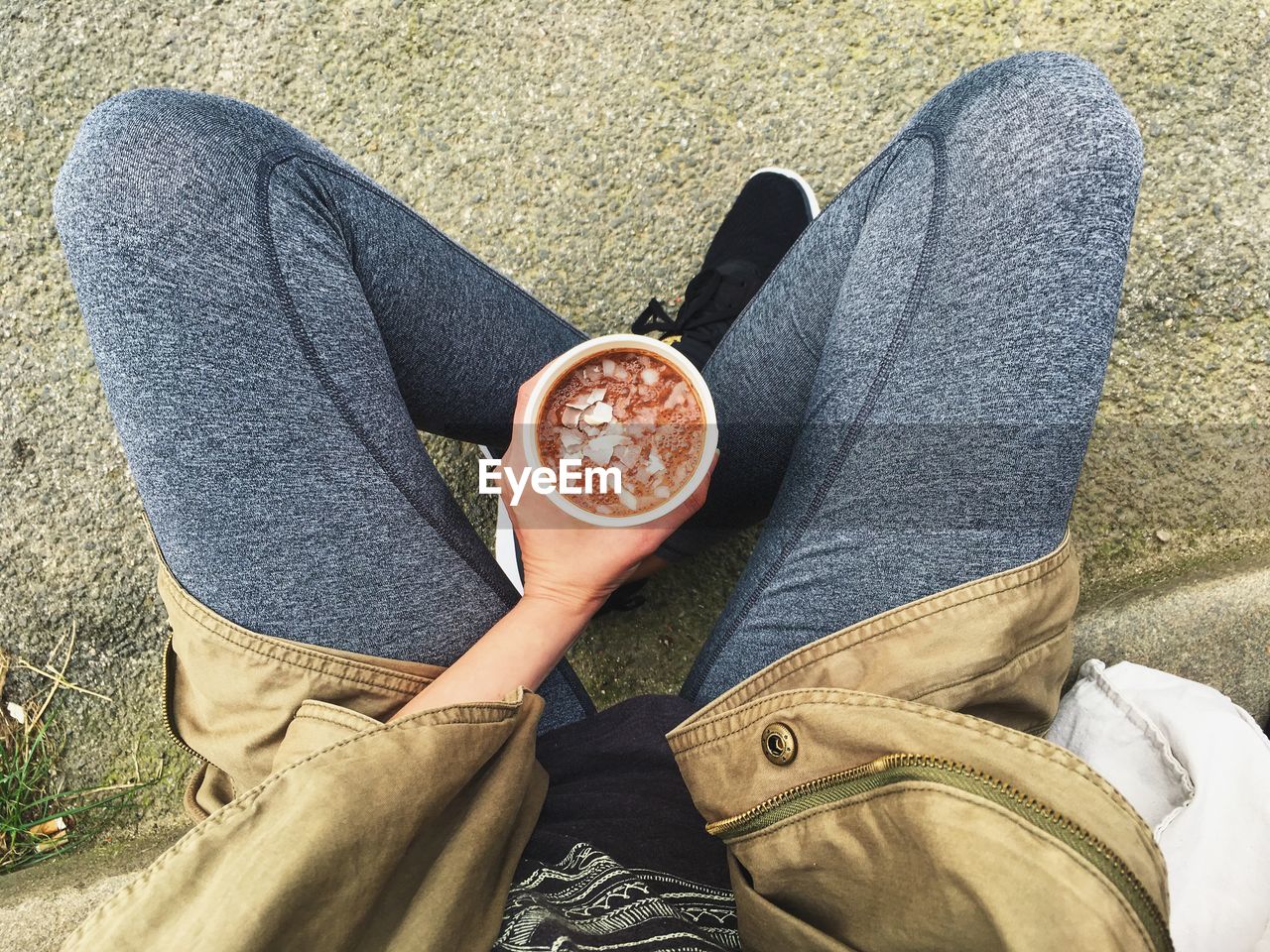 Low section of woman having smoothie while sitting on footpath