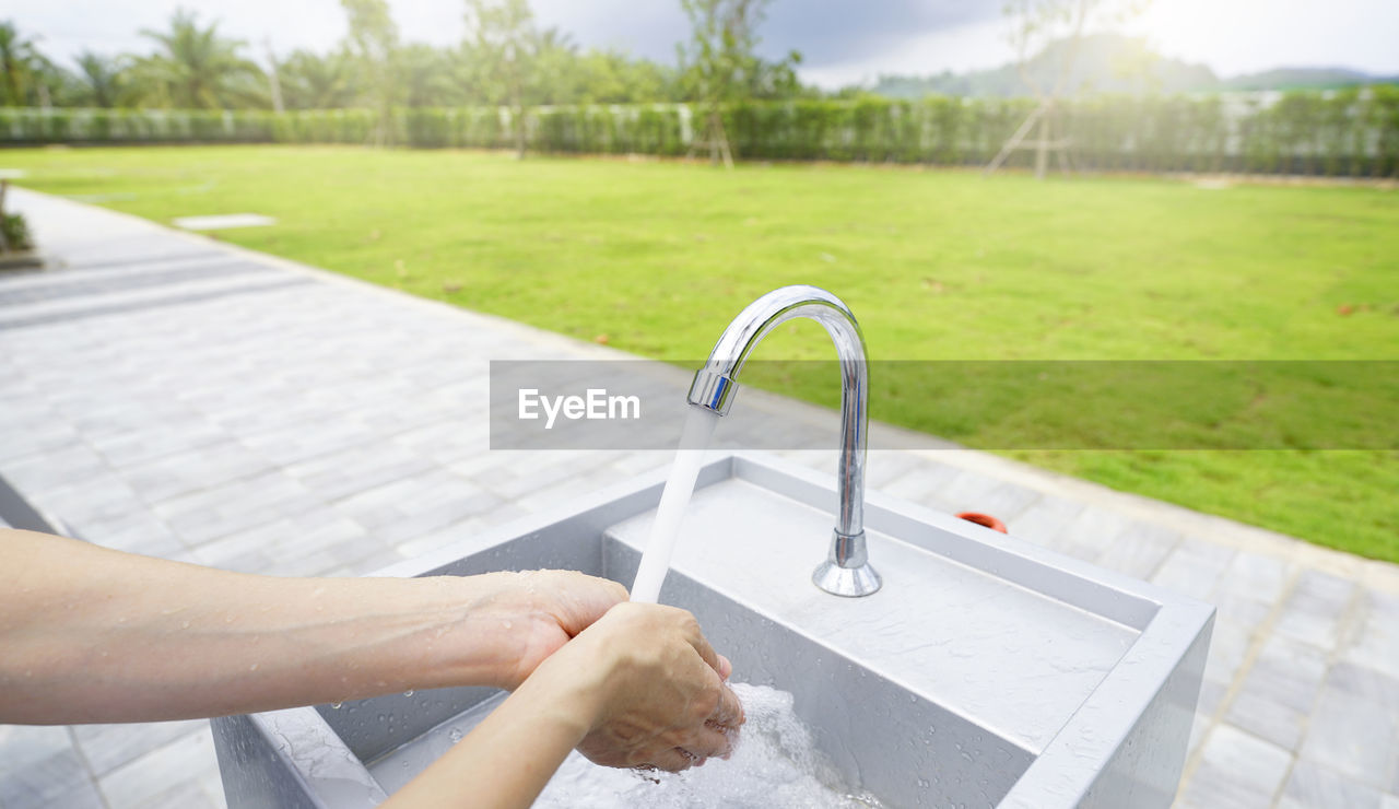 hand, nature, one person, adult, sink, lifestyles, water, tap, grass, faucet, day, plant, women, outdoors, home, domestic life, leisure activity, young adult, relaxation, holding, focus on foreground, plumbing fixture, summer, cleaning, sunlight, motion, architecture, hygiene, swimming pool, tree