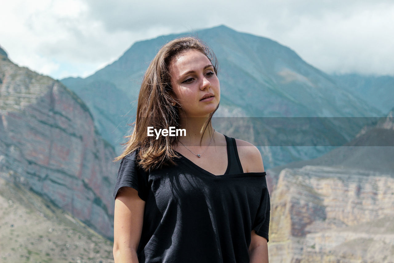 Beautiful young woman looking away while standing against mountain range