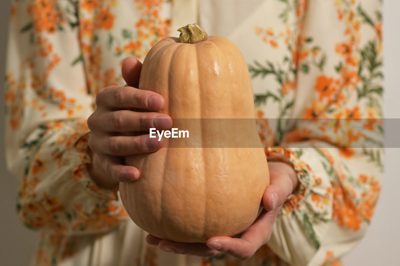 CLOSE-UP OF BABY HAND HOLDING PUMPKIN AGAINST ORANGE BACKGROUND