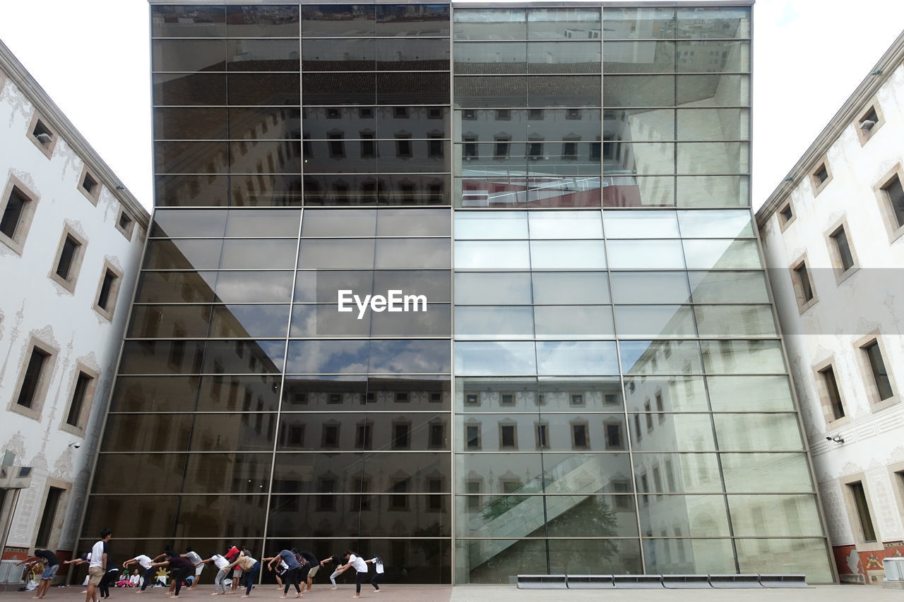 LOW ANGLE VIEW OF PEOPLE ON GLASS BUILDING