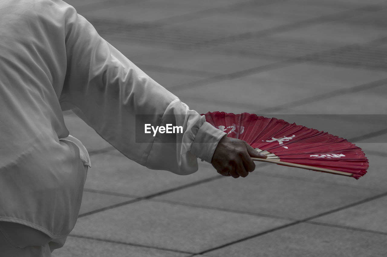 LOW SECTION OF PERSON SITTING ON FOOTPATH BY RED FLOOR