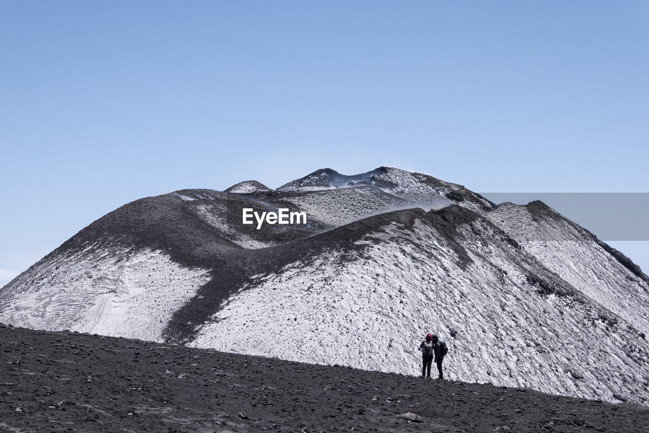 REAR VIEW OF MAN ON SNOWCAPPED MOUNTAIN AGAINST SKY