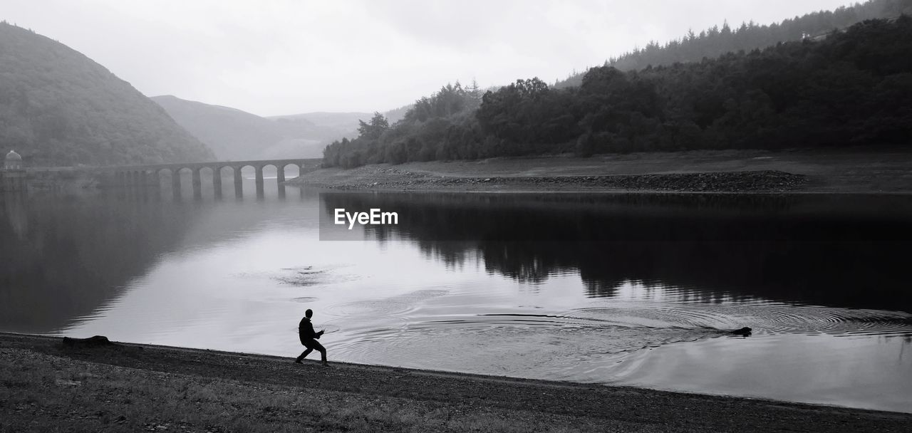 Silhouette man standing by river against sky