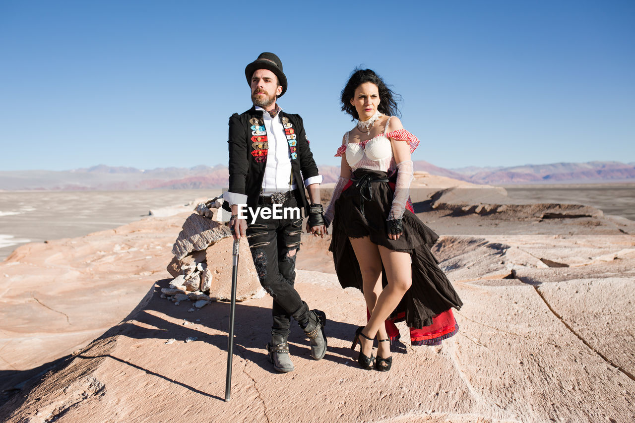 FULL LENGTH PORTRAIT OF YOUNG WOMAN ON DESERT AGAINST SKY