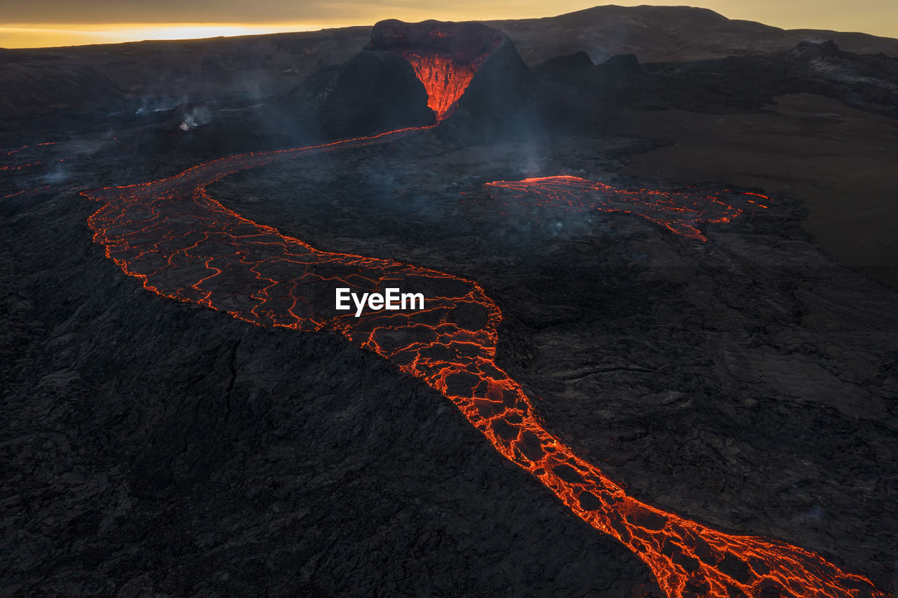 Drone view of stream of hot orange lava flowing through mountainous terrain in morning in iceland