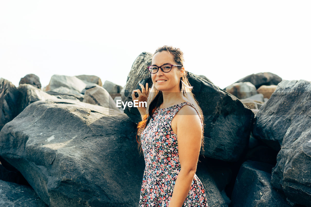 Portrait of woman standing by rock against sky