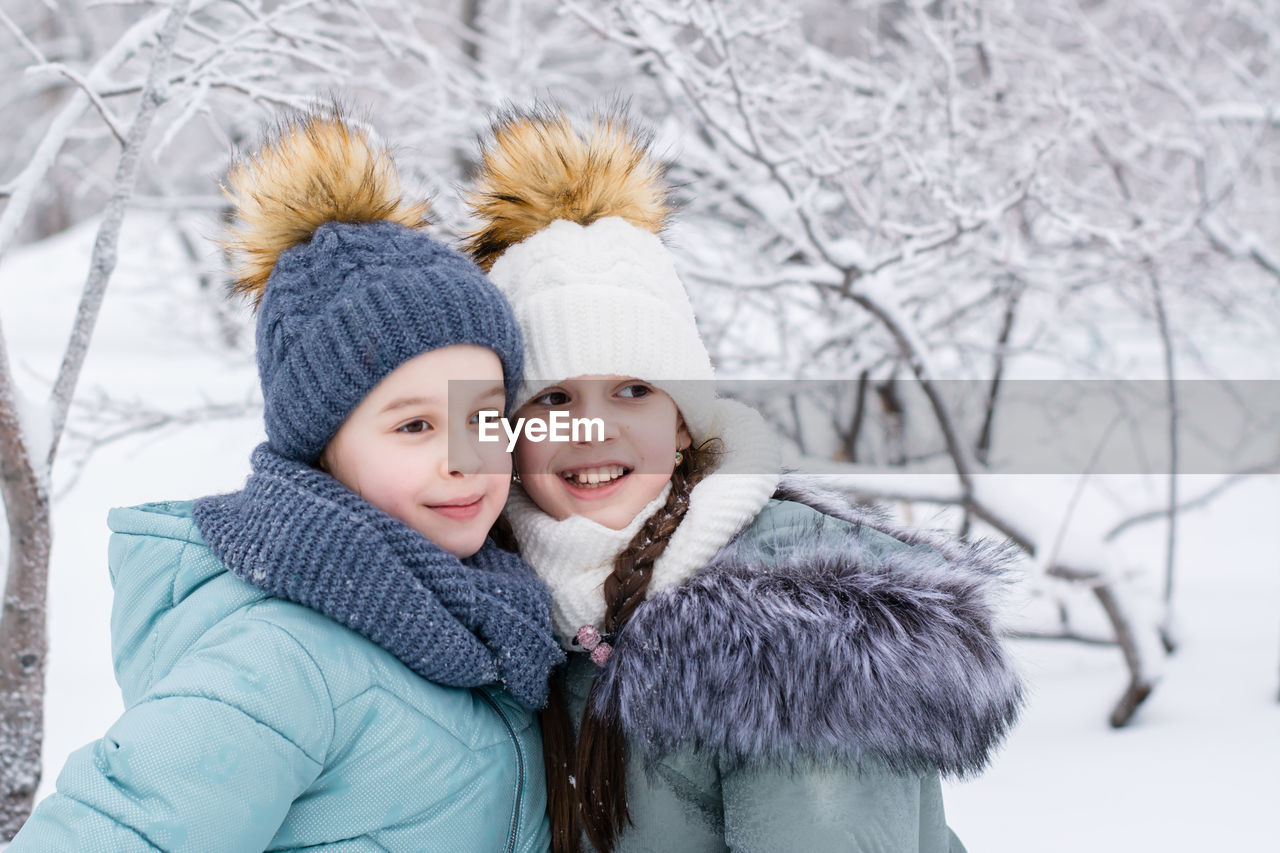 Two smiling girls in warm clothes are hugging in a snowy park. winter walks, lifestyle