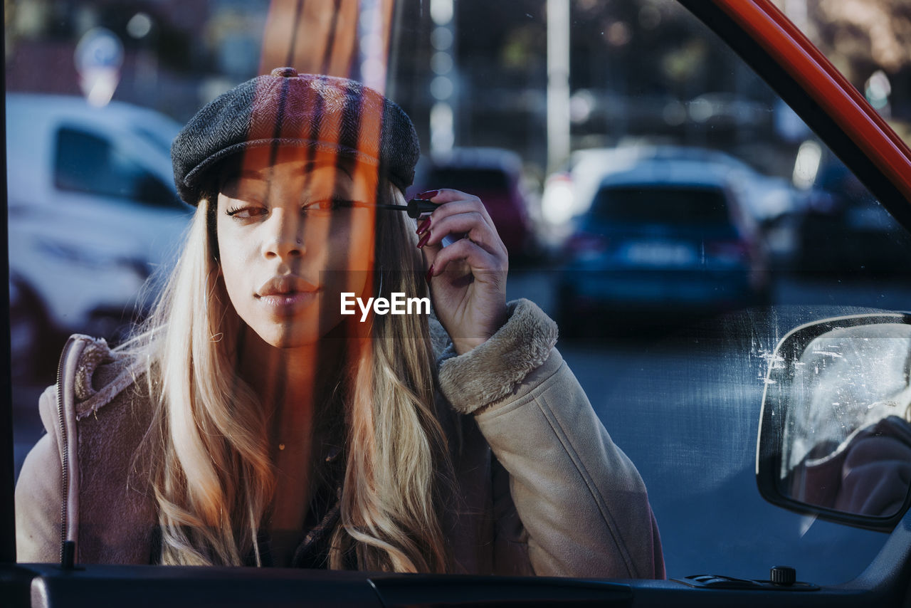 Ethnic female applying makeup near car