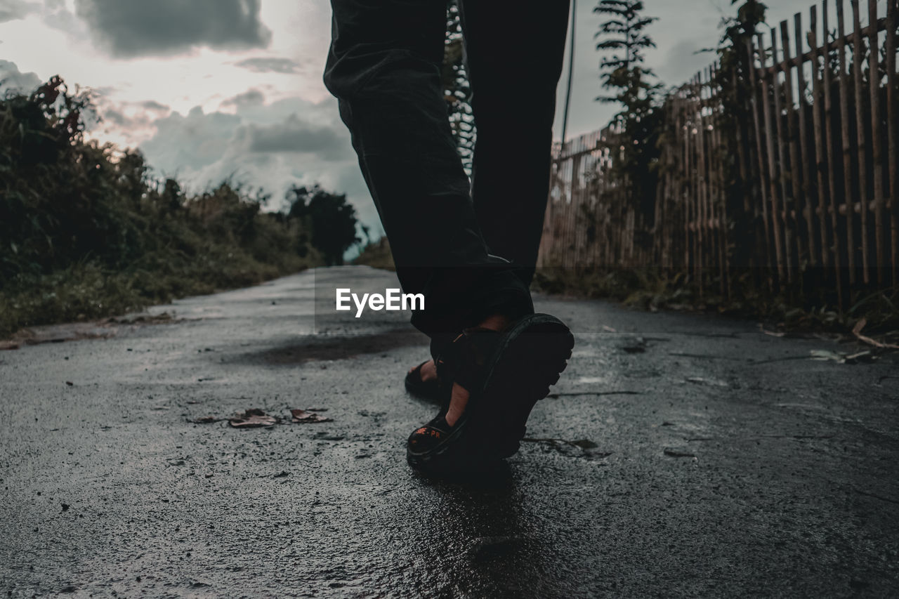  low section of man standing on road after rain and twilight comes 