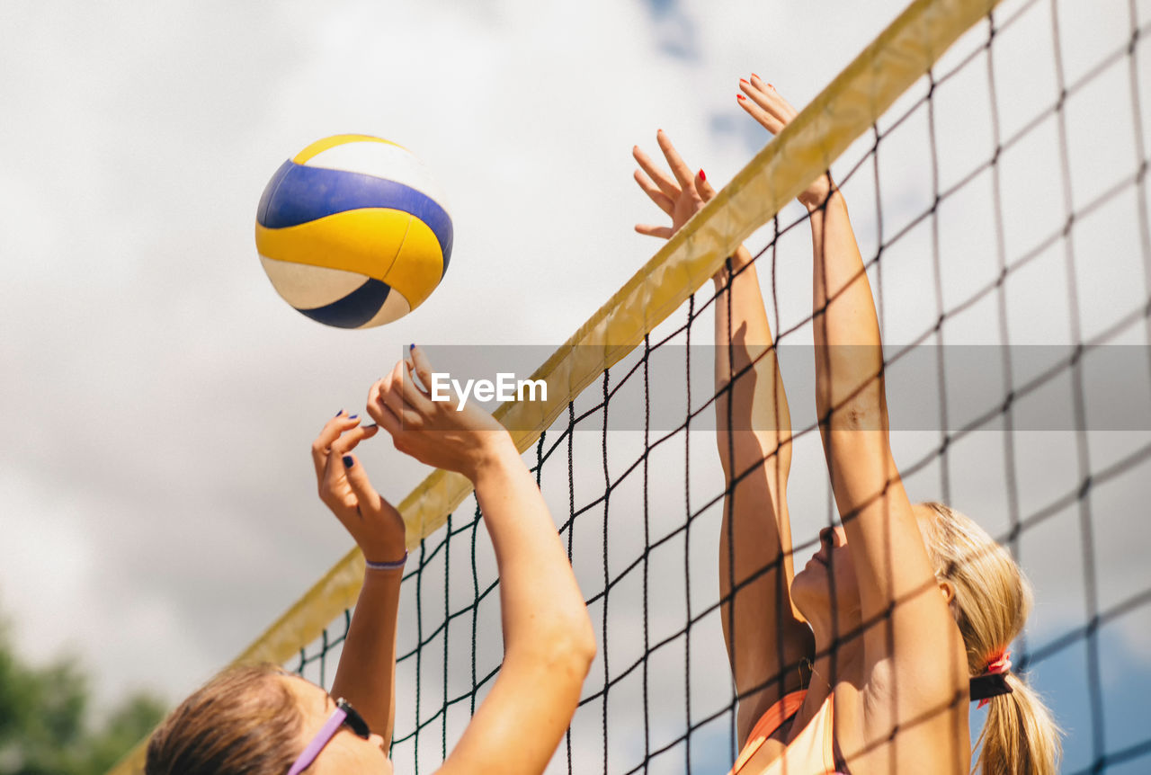 Low angle view of women playing beach volleyball against sky