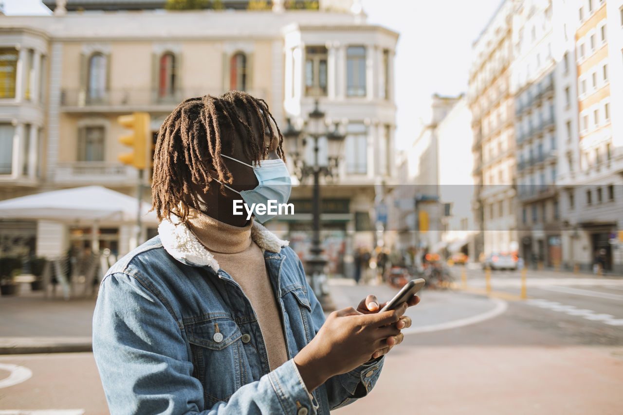 Young man with smart phone standing in city during coronavirus