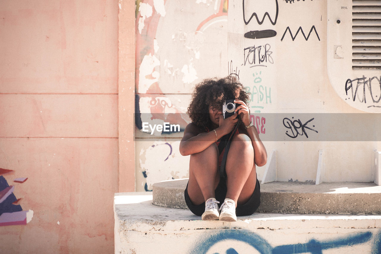 FULL LENGTH OF WOMAN SITTING BY WALL