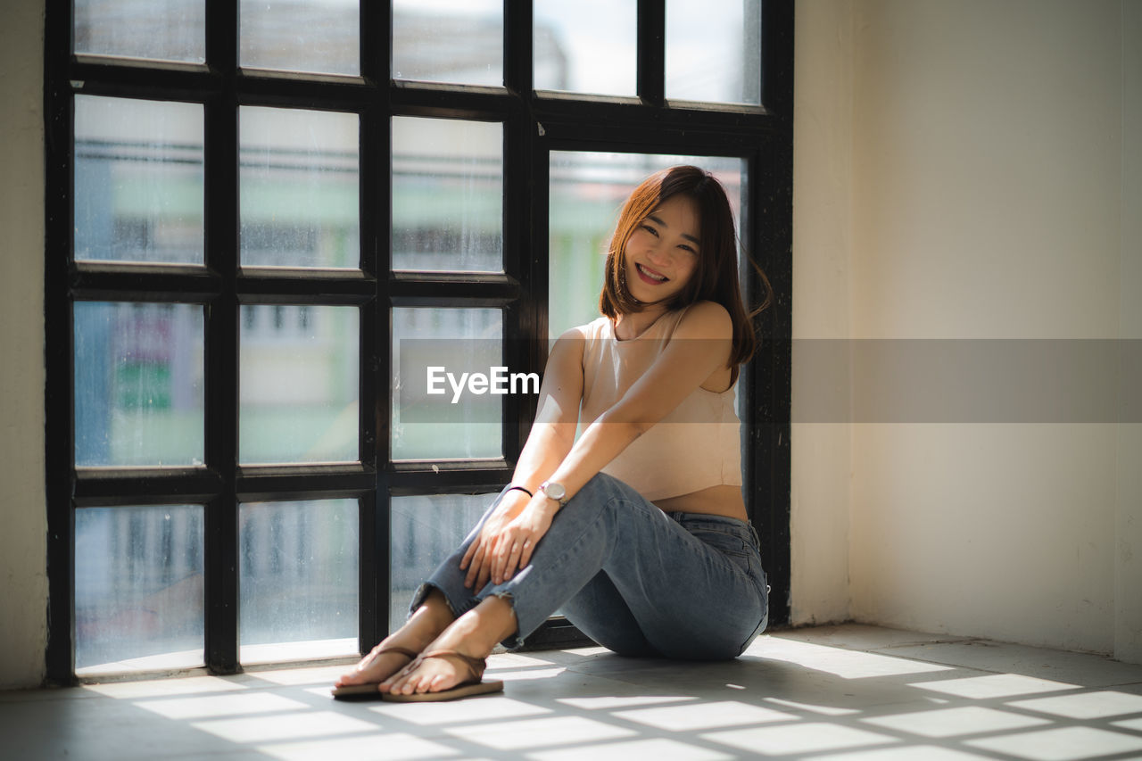 Portrait of young woman sitting on window at home