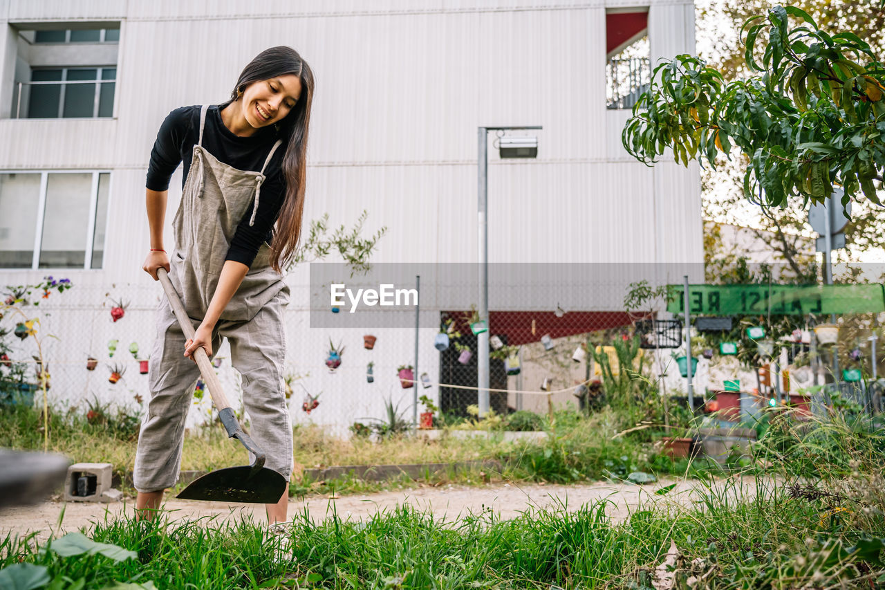 Happy young woman gardening with shovel in urban garden