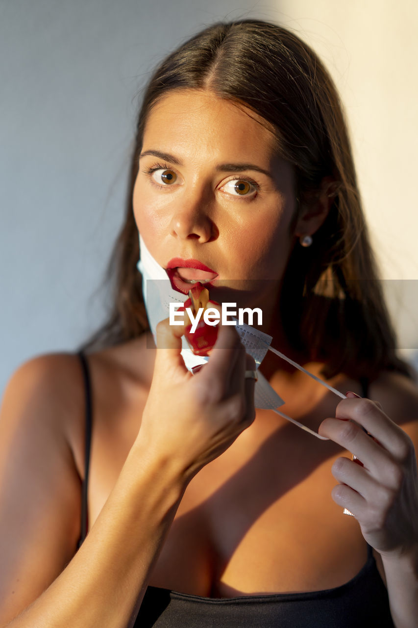 Young woman painting her lips red with a face mask. new normal concept