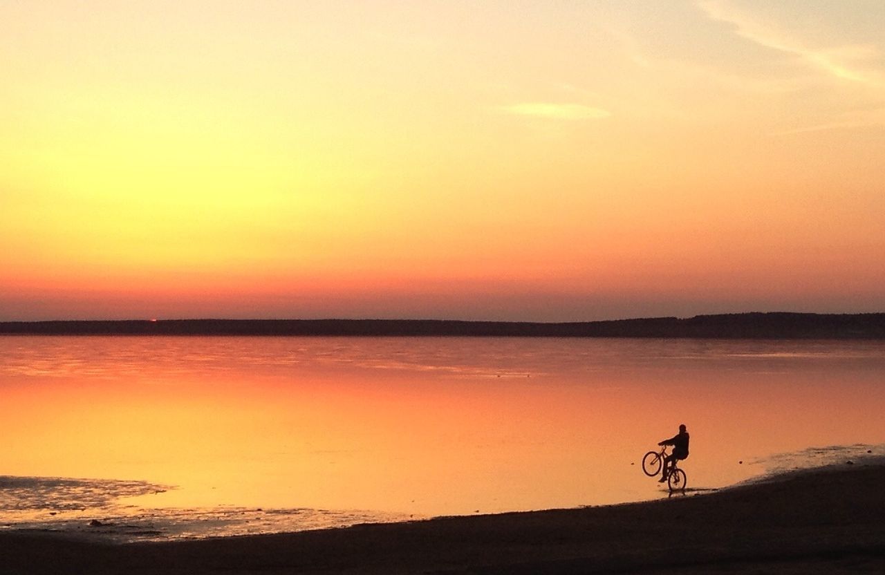 Silhouette person bicycling on calm beach at sunset