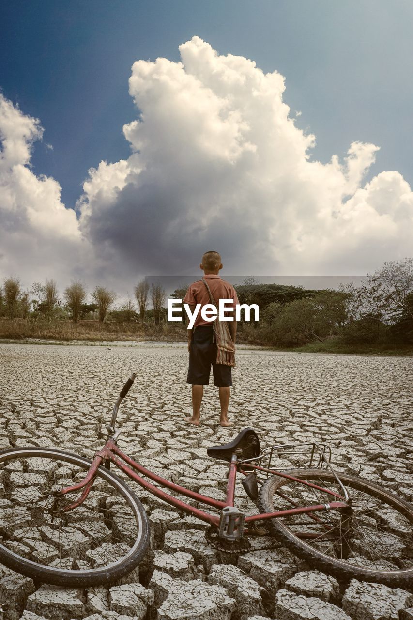 Rear view of boy standing on dry land against cloudy sky