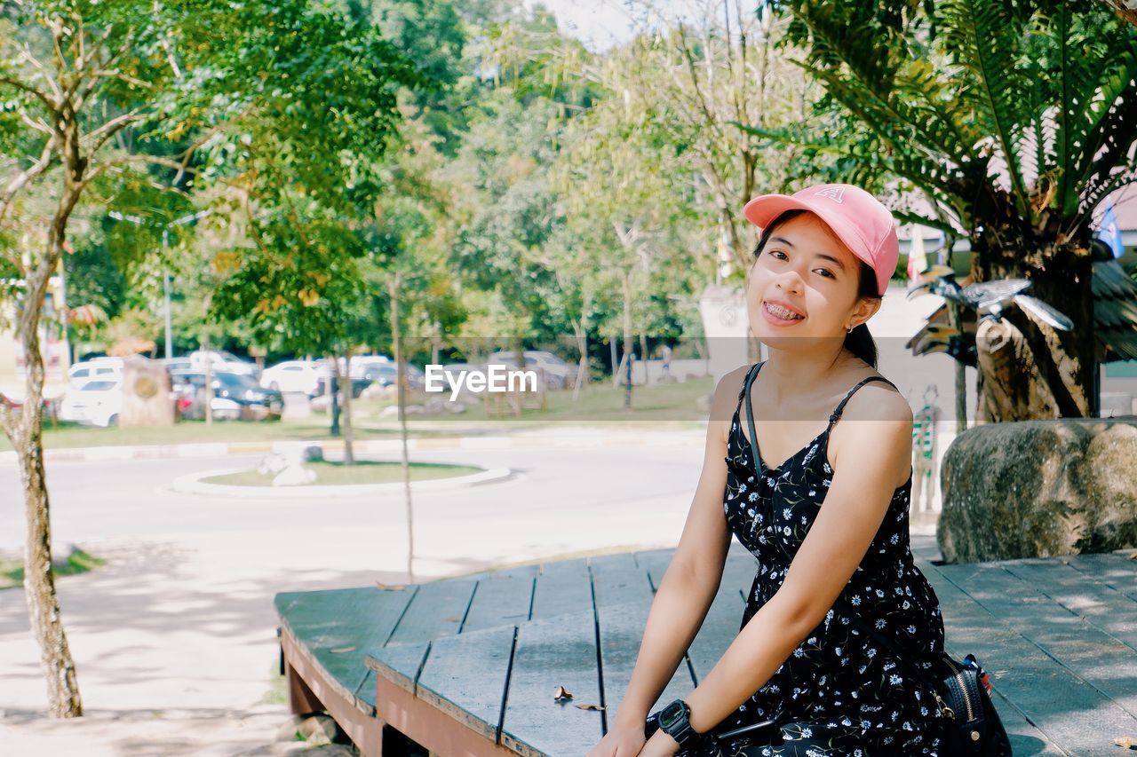 PORTRAIT OF SMILING YOUNG WOMAN WITH HAT ON TREES