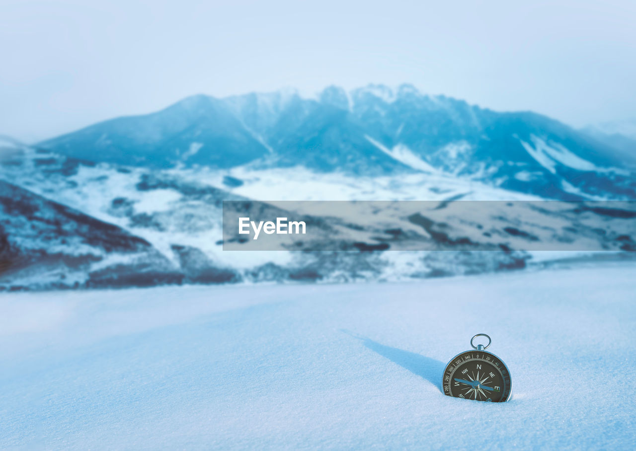 Navigational compass on snow covered field against mountains