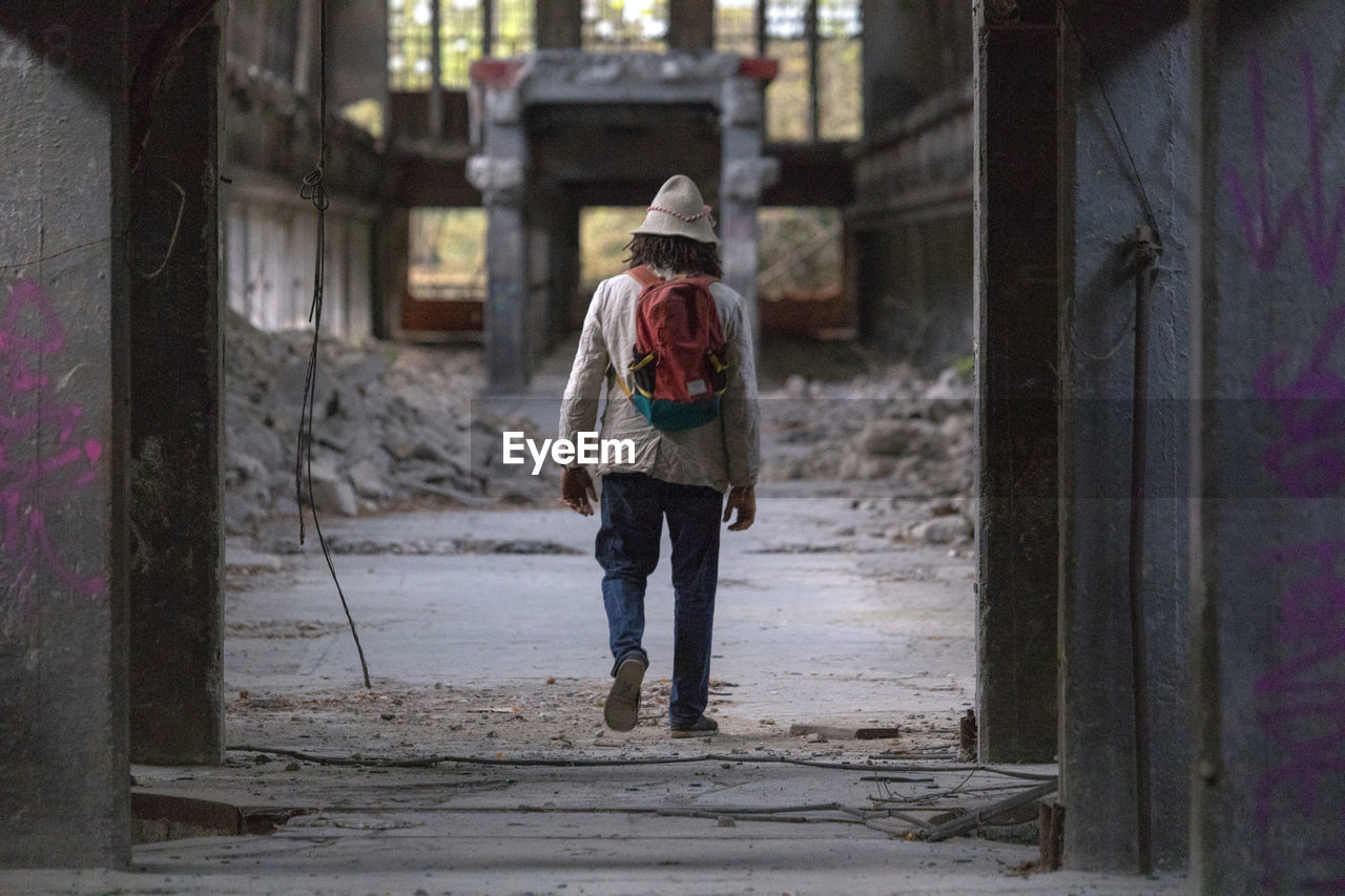 FULL LENGTH REAR VIEW OF MAN WALKING IN ABANDONED BUILDING