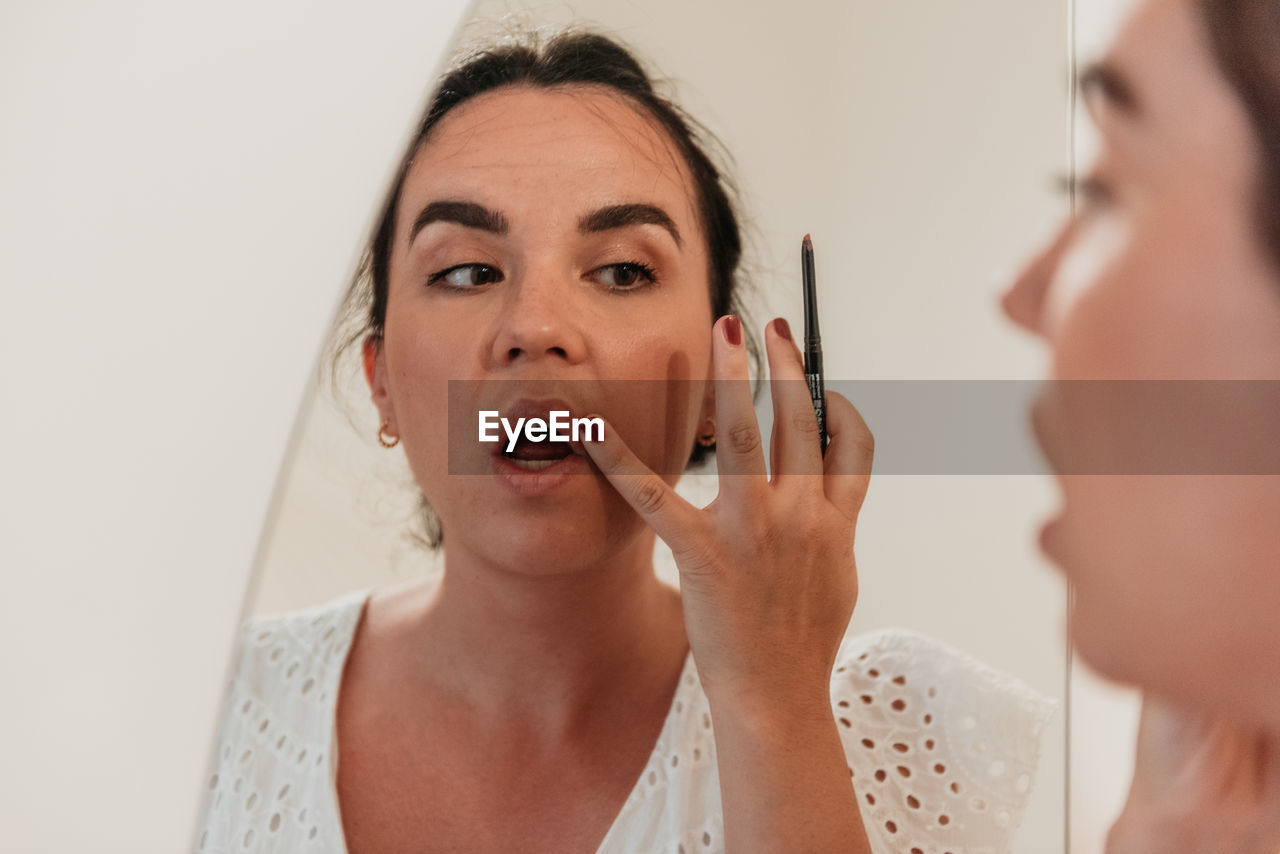 Mirror photo of beautiful young woman putting on makeup