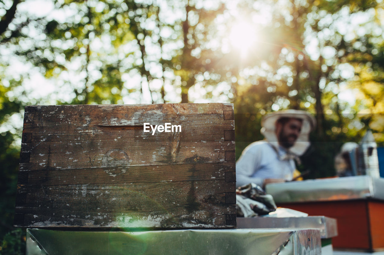 Close-up of container with beekeeper in background