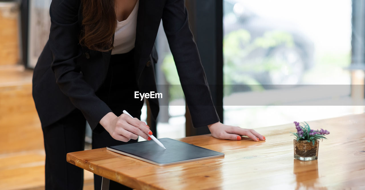 Close up view of business woman holding stylus pen and using digital tablet on wooden desk at cafe.