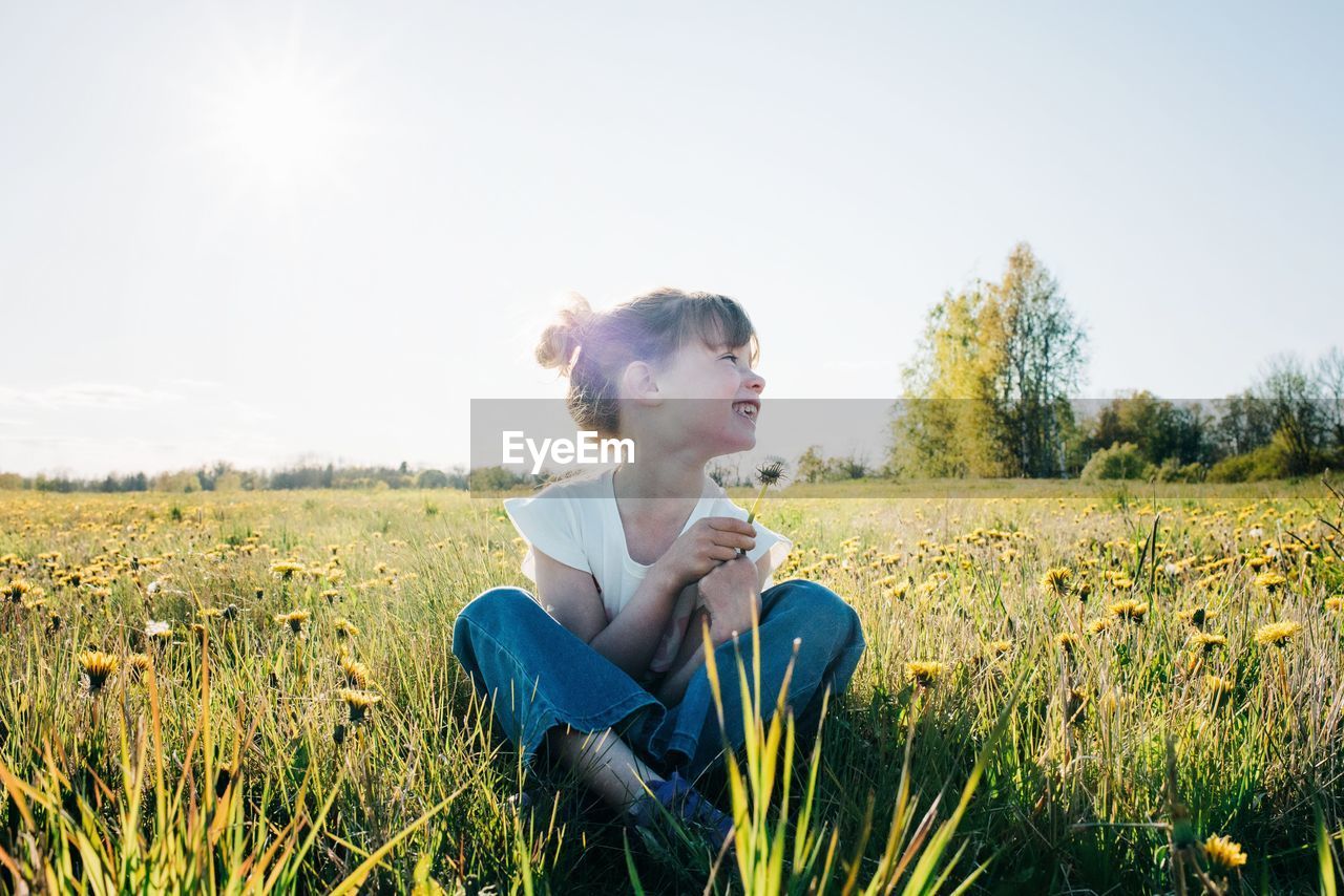 Portrait of a young girl sat in a yellow flower field in summer