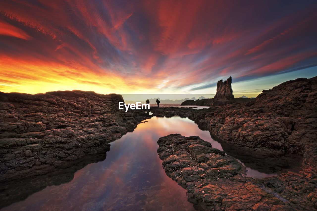 Rocks in sea against sky during sunset