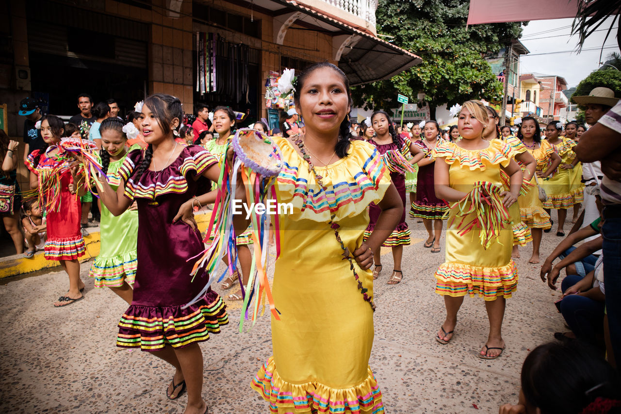 HAPPY YOUNG WOMAN STANDING AGAINST MULTI COLORED TRADITIONAL CLOTHING