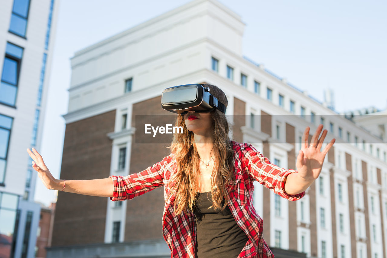 Woman wearing virtual reality simulator against building