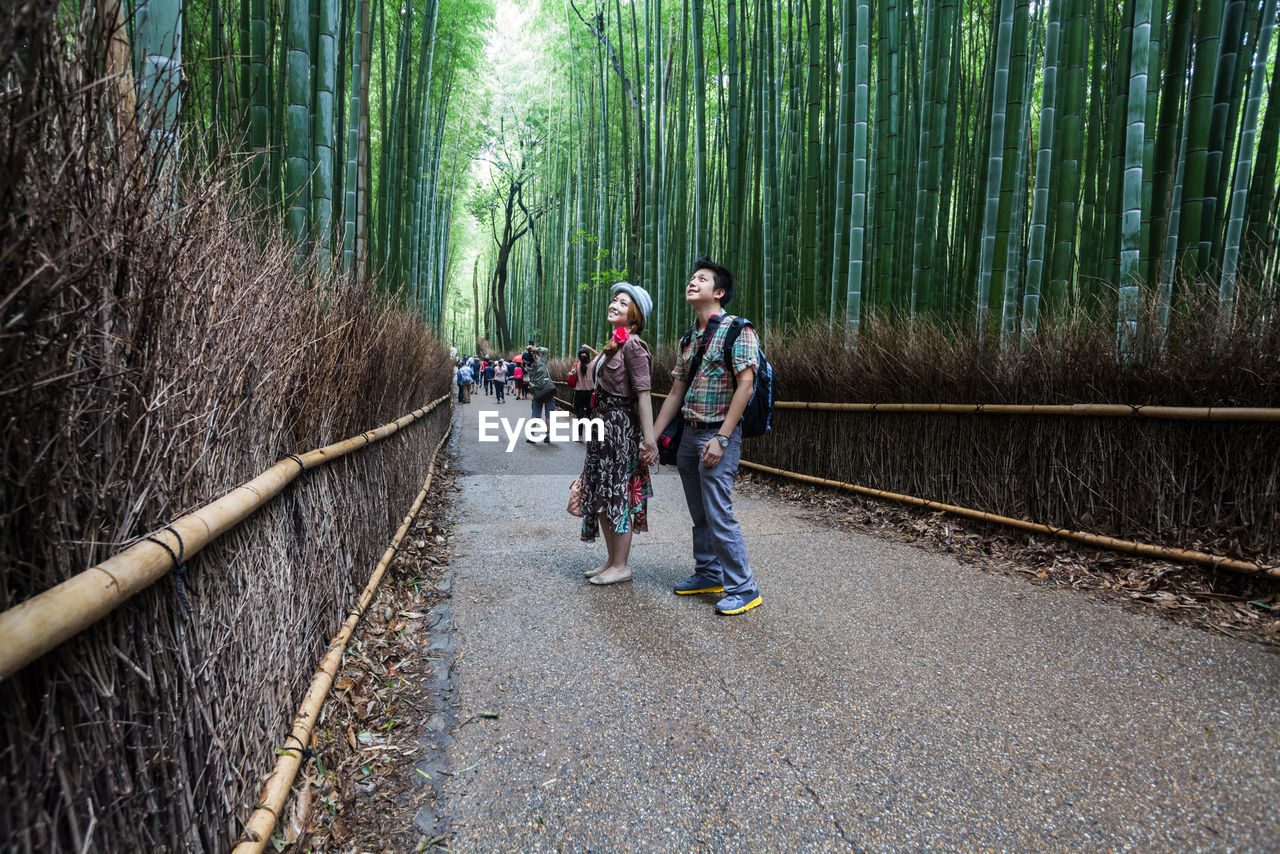 Smiling couple standing on pathway amidst bamboos at arashiyama