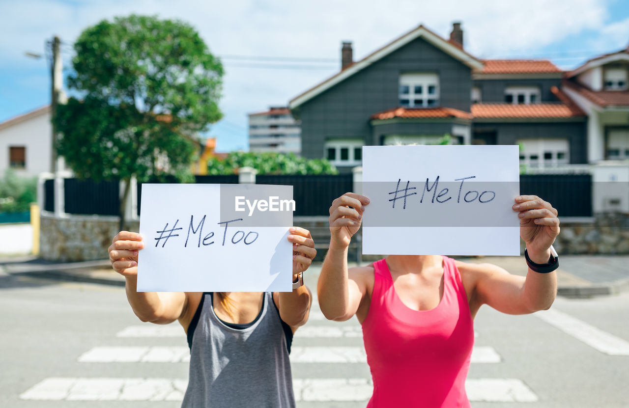 Women covering face with placard while standing on city street