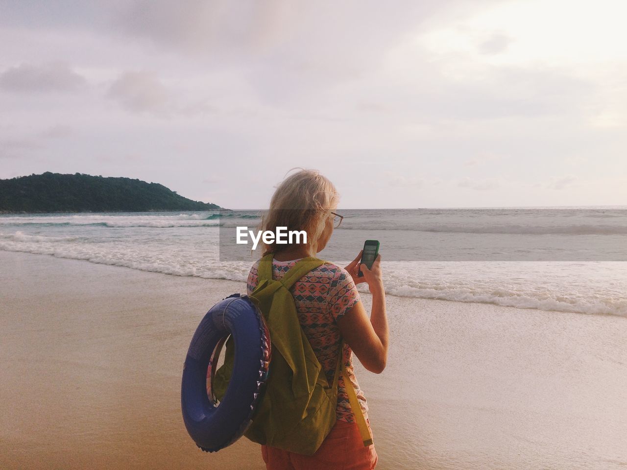 Woman using mobile phone while standing against sea at beach