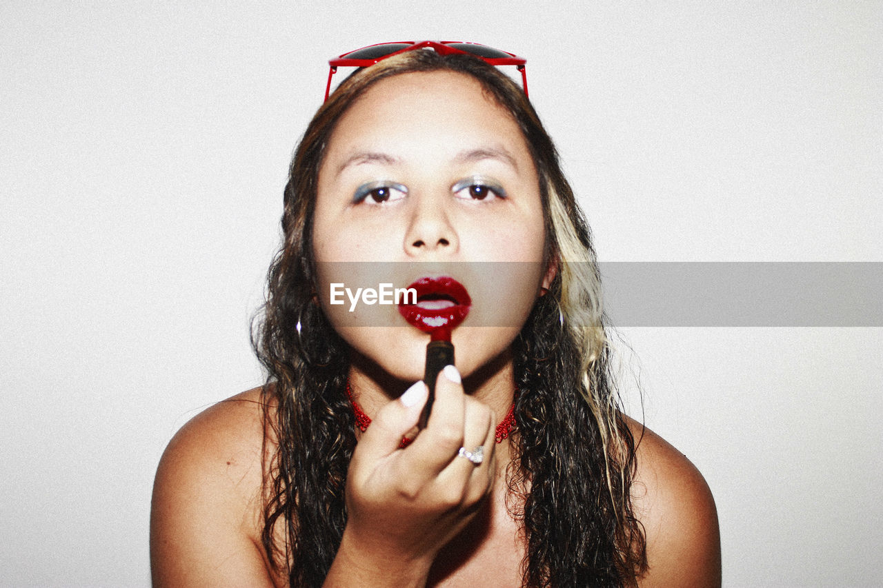 Close-up portrait of woman applying red lipstick against white background