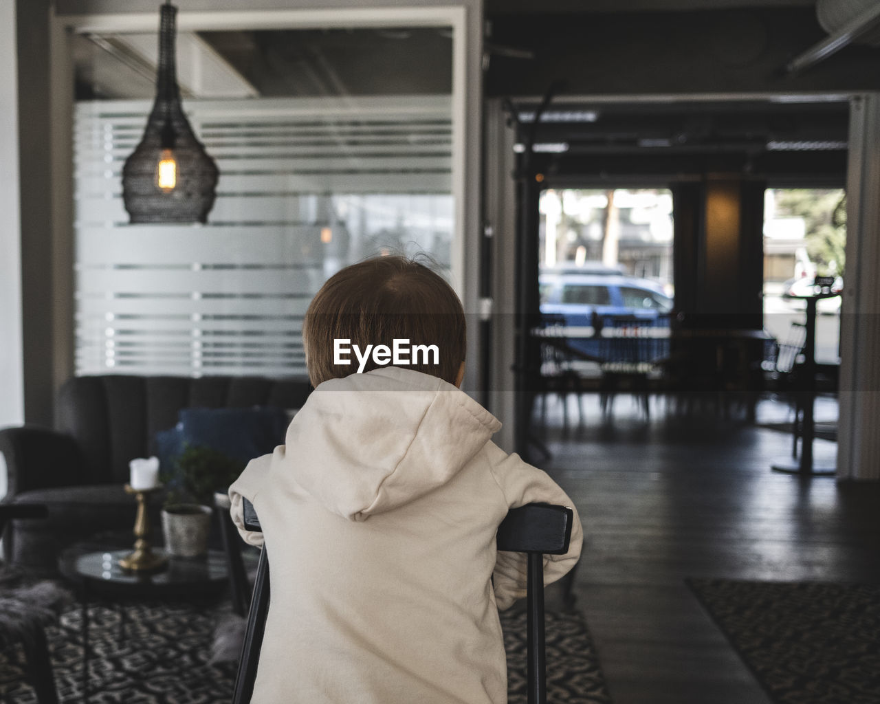 Rear view of boy wearing hooded jacket while leaning on chair in cafe