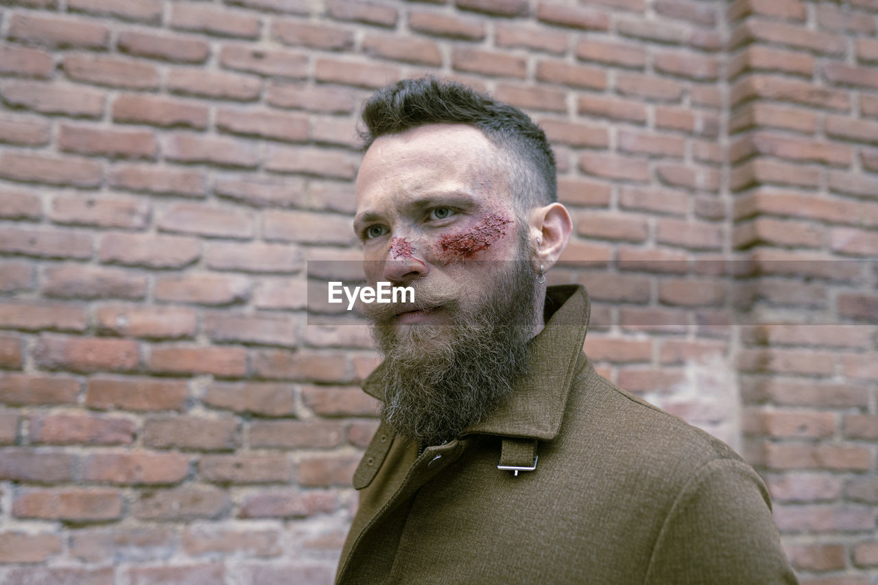 Side view hipster man with beard and cinema makeup posing on the street